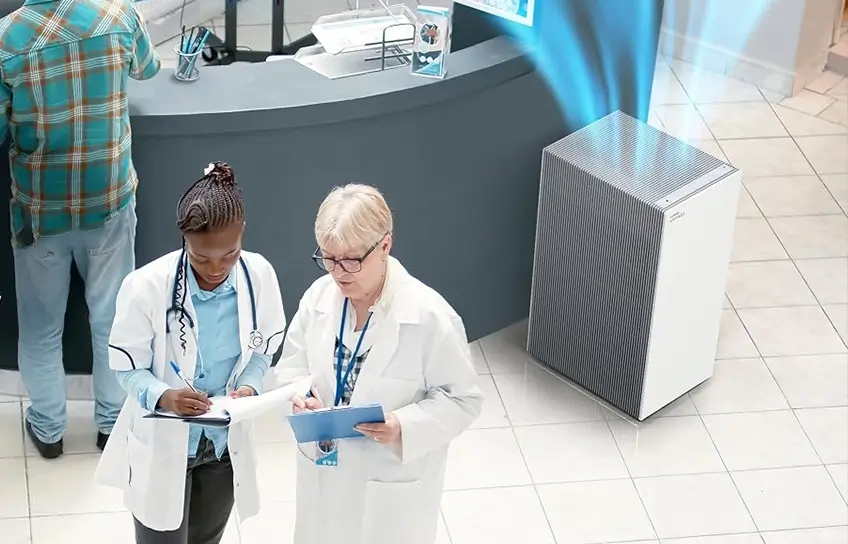 Coway Airmega ProX air purifier running in a busy medical office reception area with staff and patients nearby